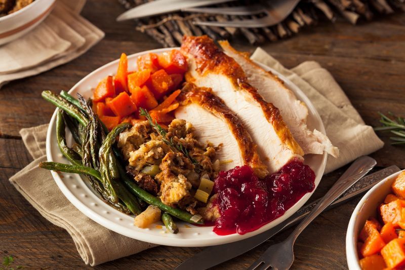 A white plate topped with turkey , stuffing , green beans , carrots and cranberry sauce.