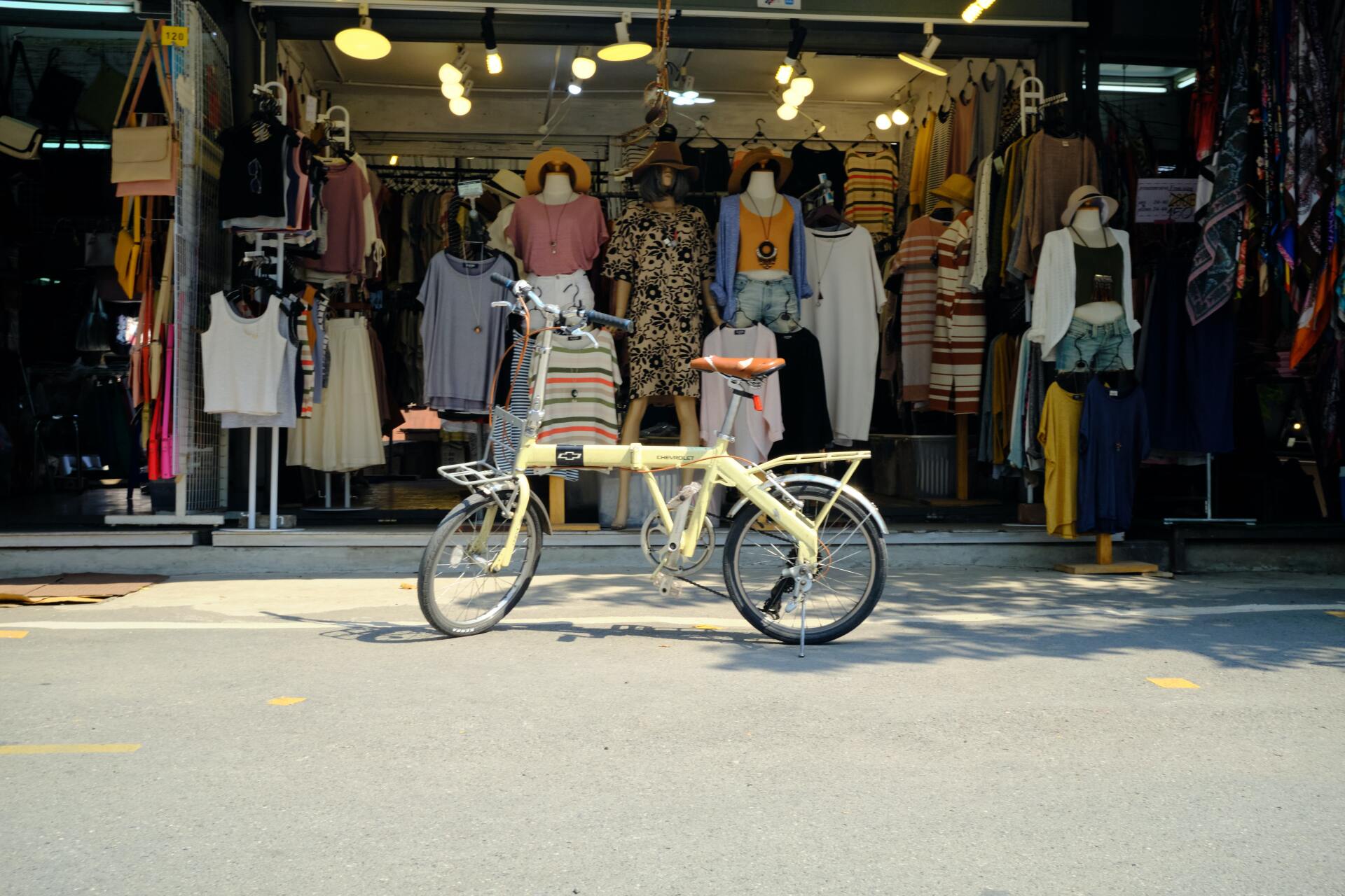 A yellow bicycle is parked in front of a clothing store.