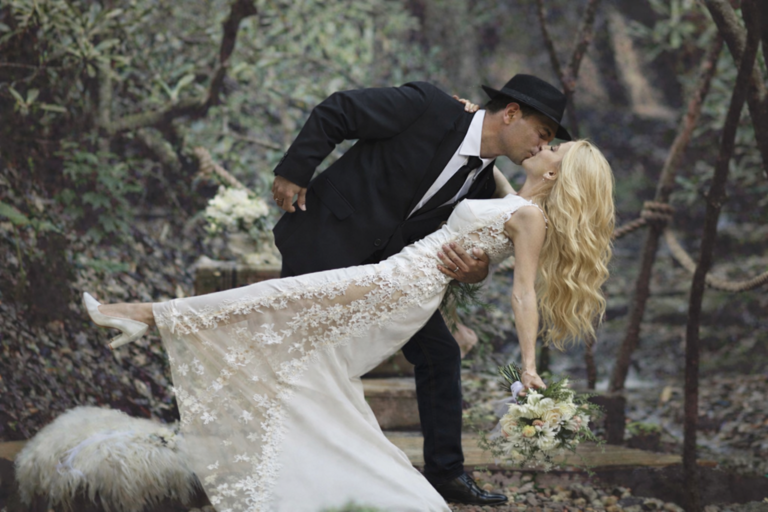 Couple embraces in a sunny forest. Bride wears white dress and headpiece, groom in a suit.
