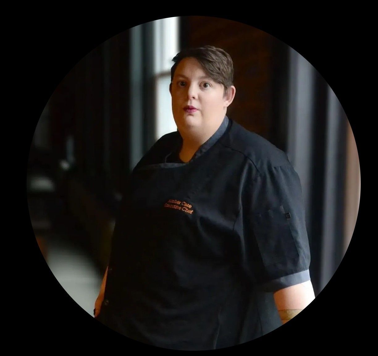 Person wearing a black uniform, standing in a dim hallway.