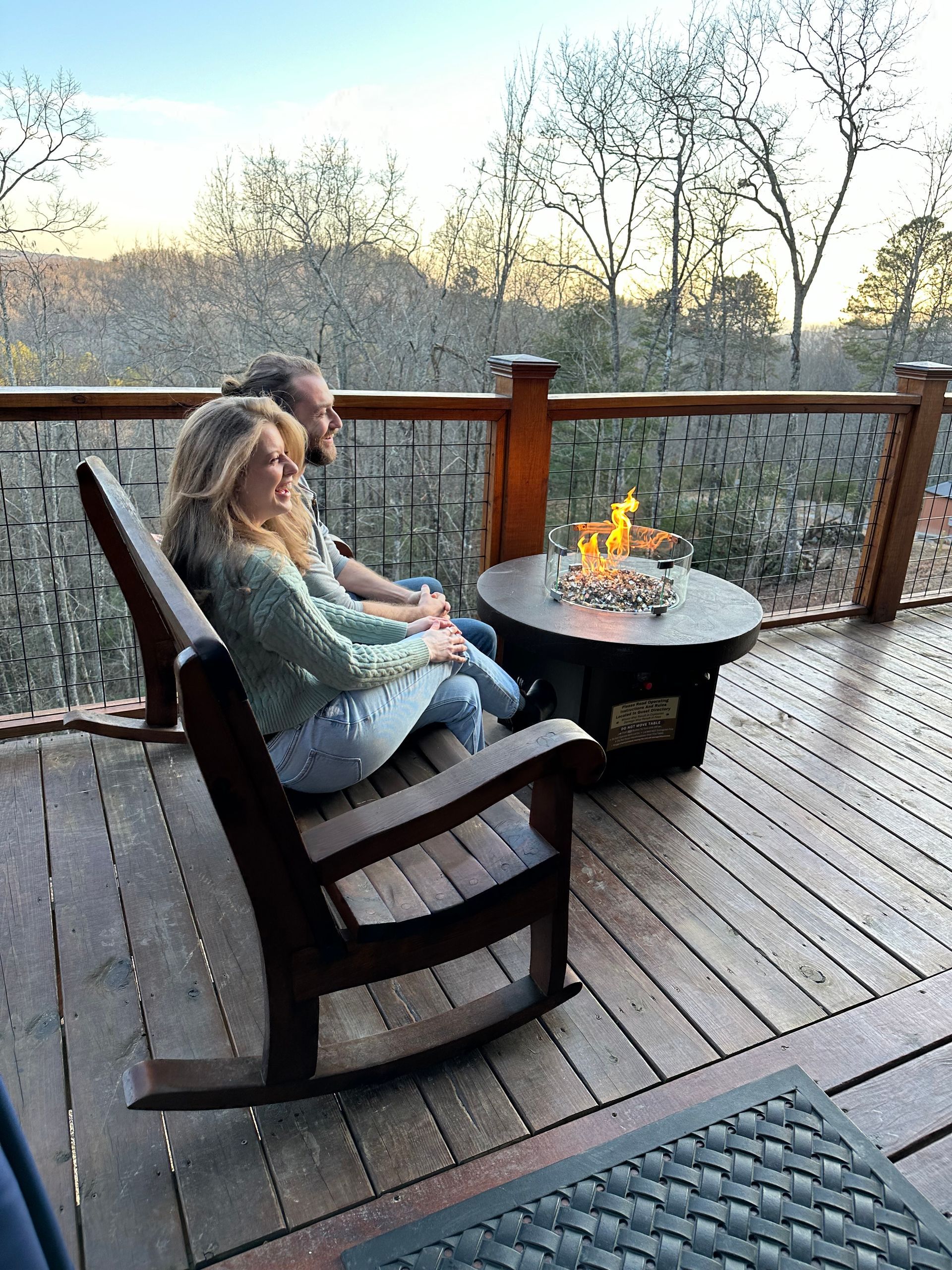 A man and a woman are sitting on a deck next to a fire pit.