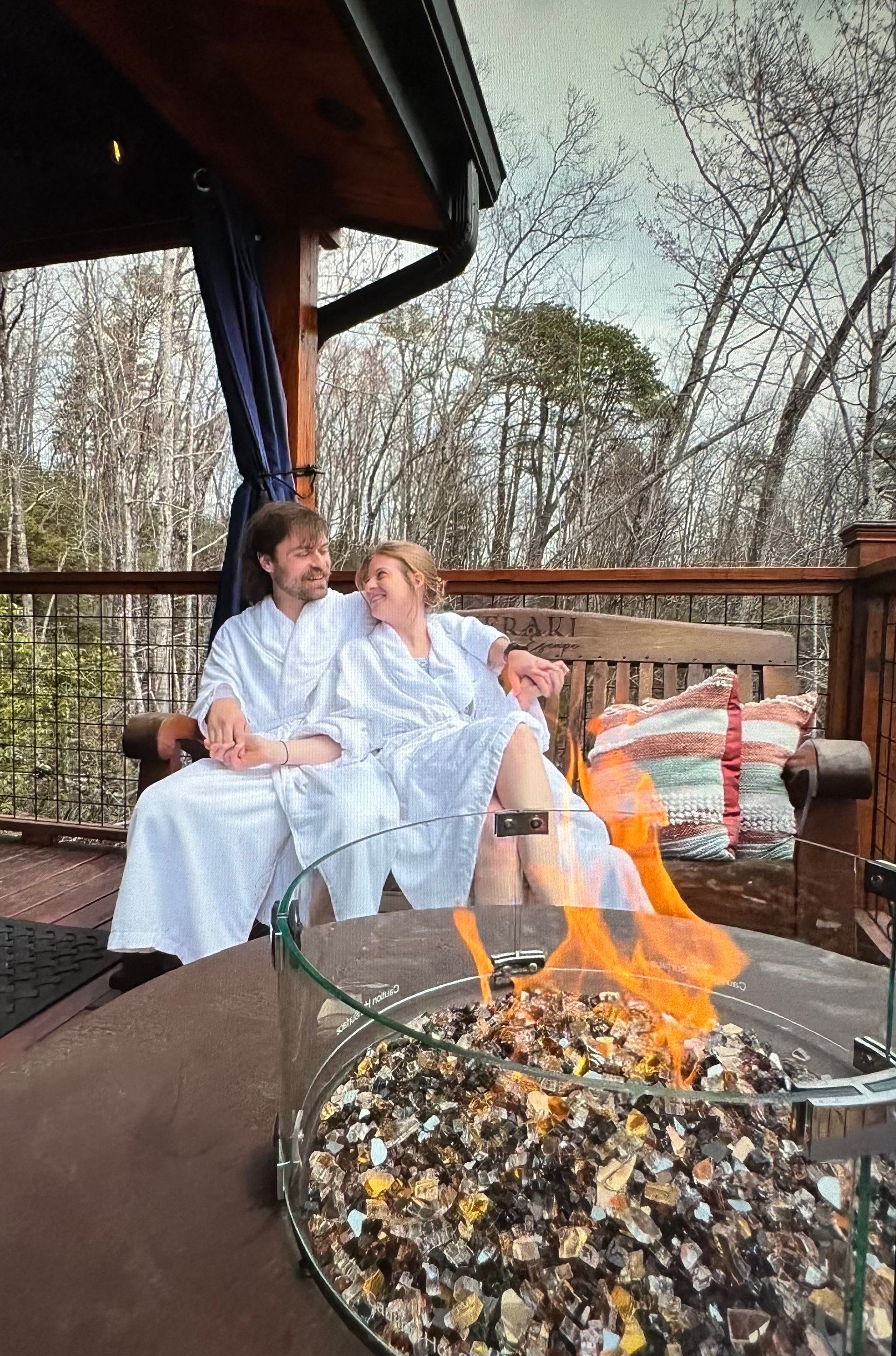 A man and a woman are sitting on a bench next to a fire pit.
