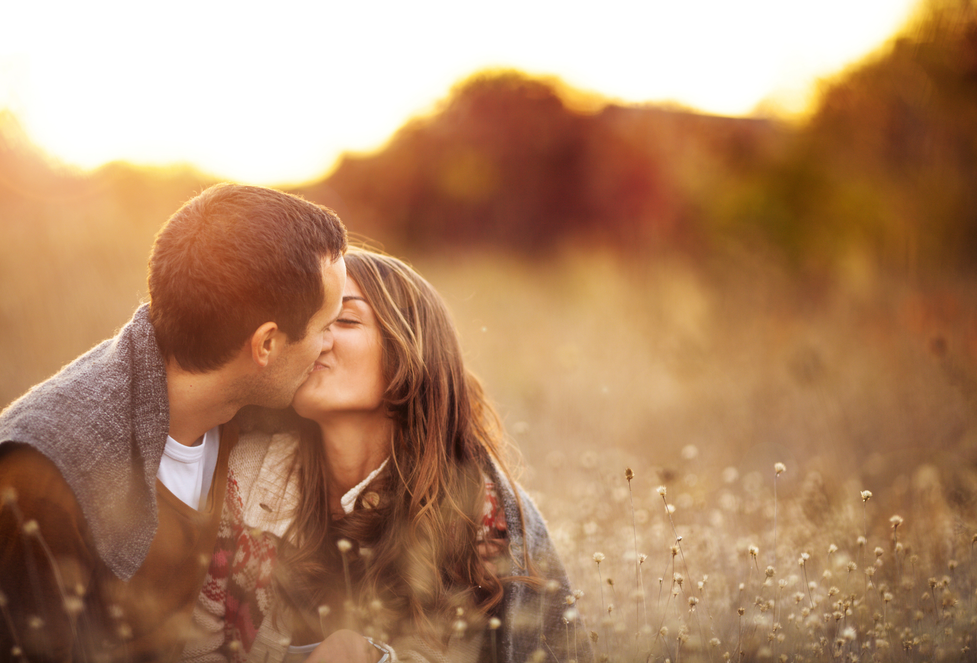 Couple wrapped in a gray blanket, smiling, standing outdoors.