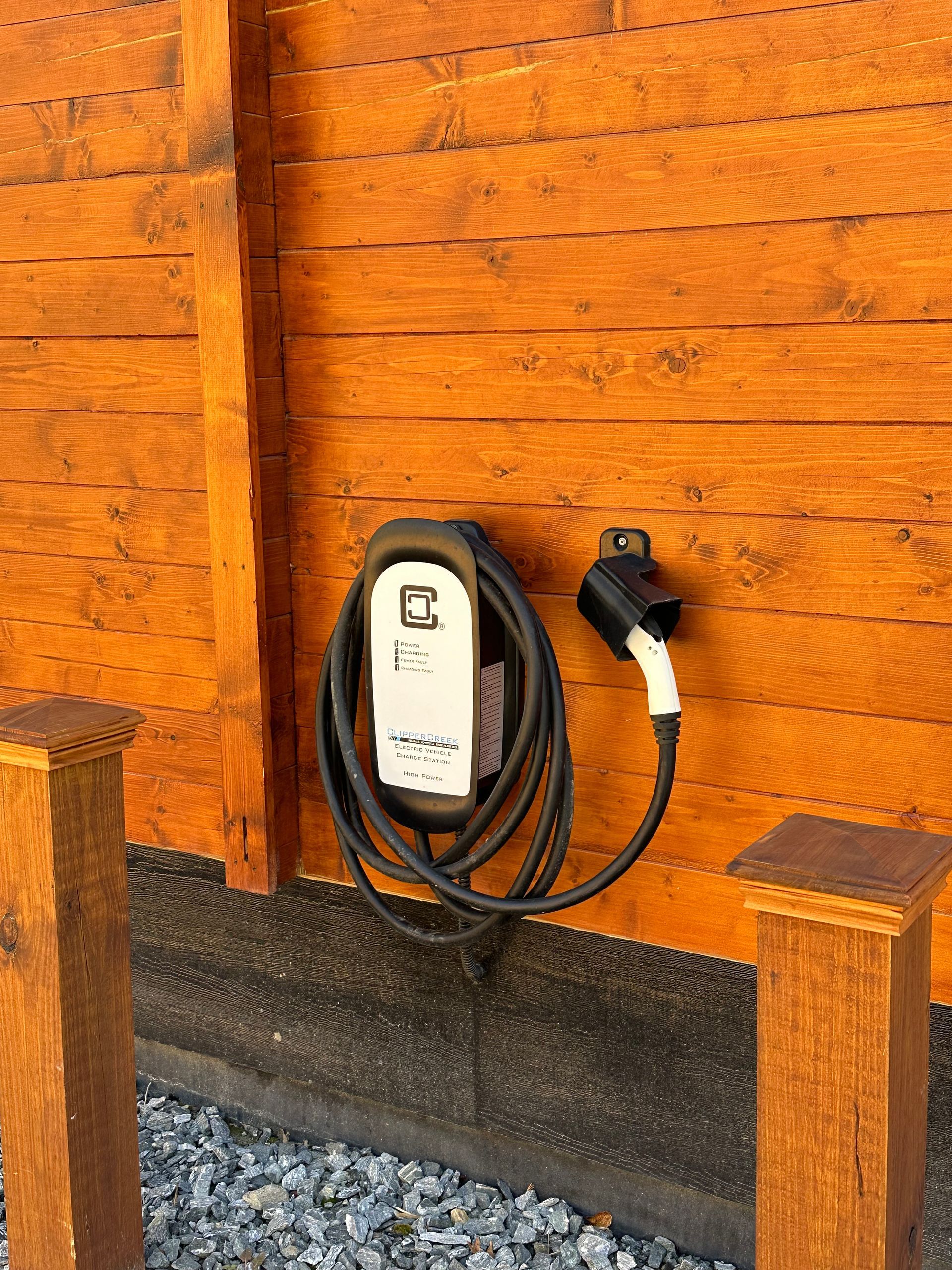 Electric vehicle charger mounted on a wooden wall. Black cable and white charging head.