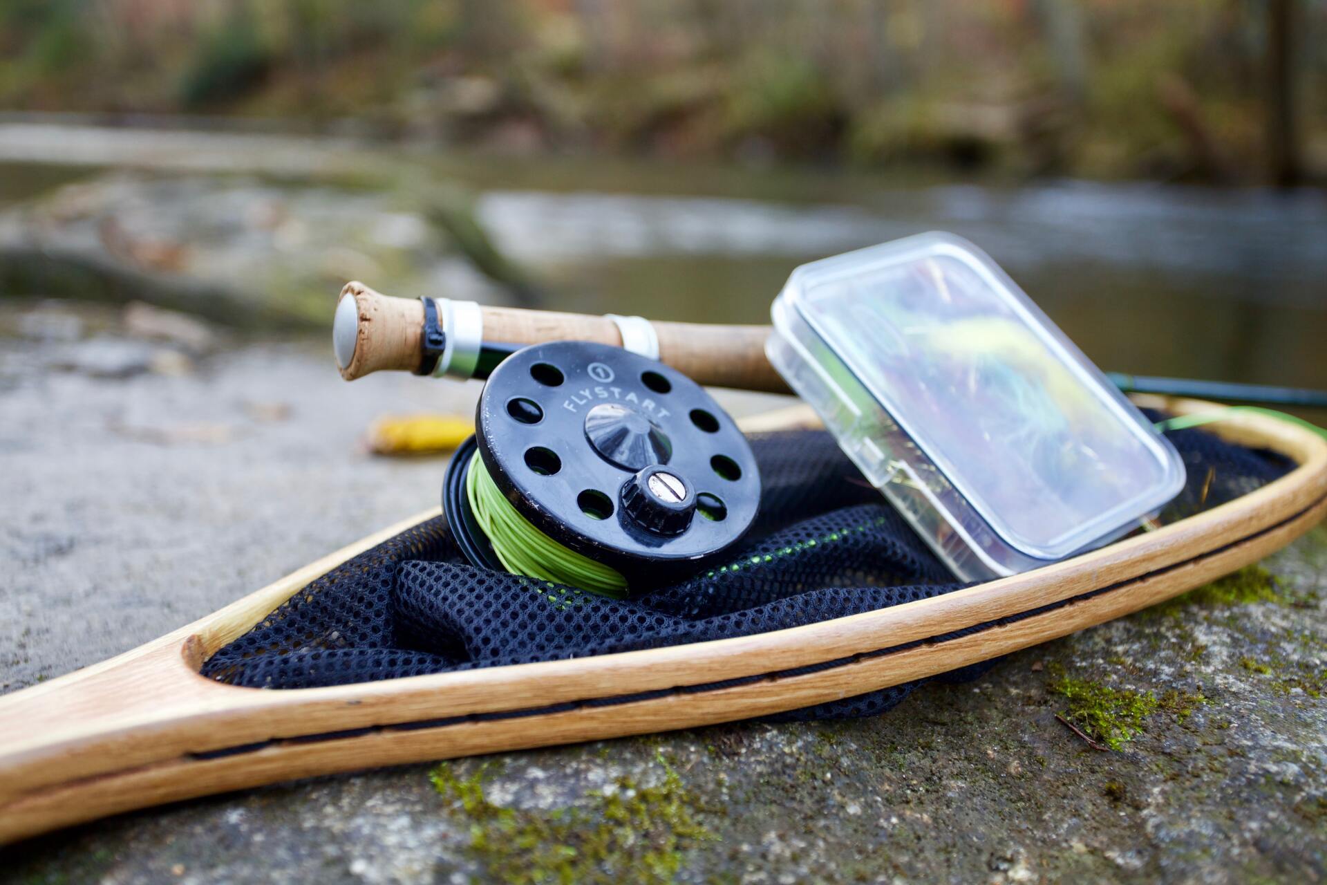 A fly fishing rod and reel are sitting on top of a wooden net.