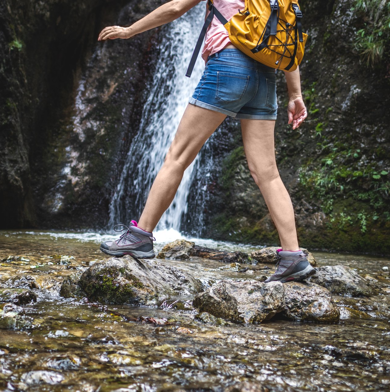 a woman with a backpack is standing in front of a waterfall