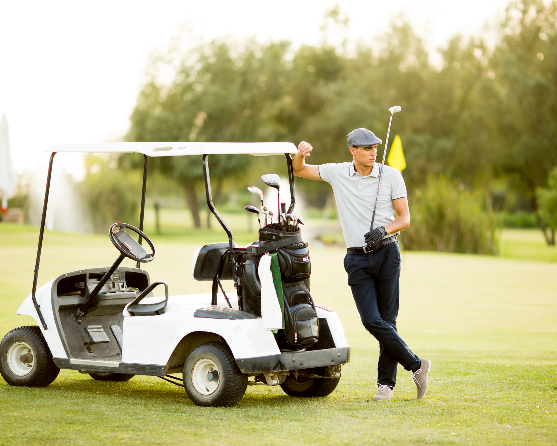 A man is standing next to a golf cart on a golf course.