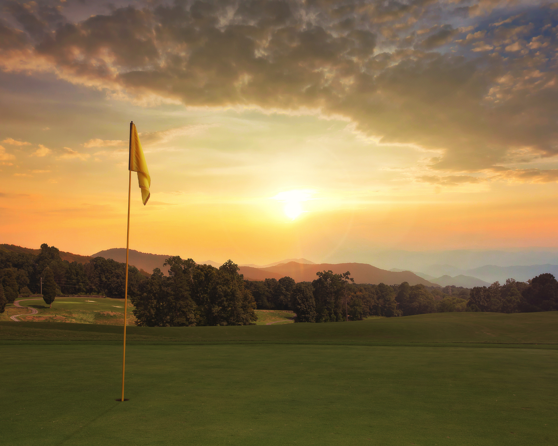 A yellow flag on a golf course at sunset