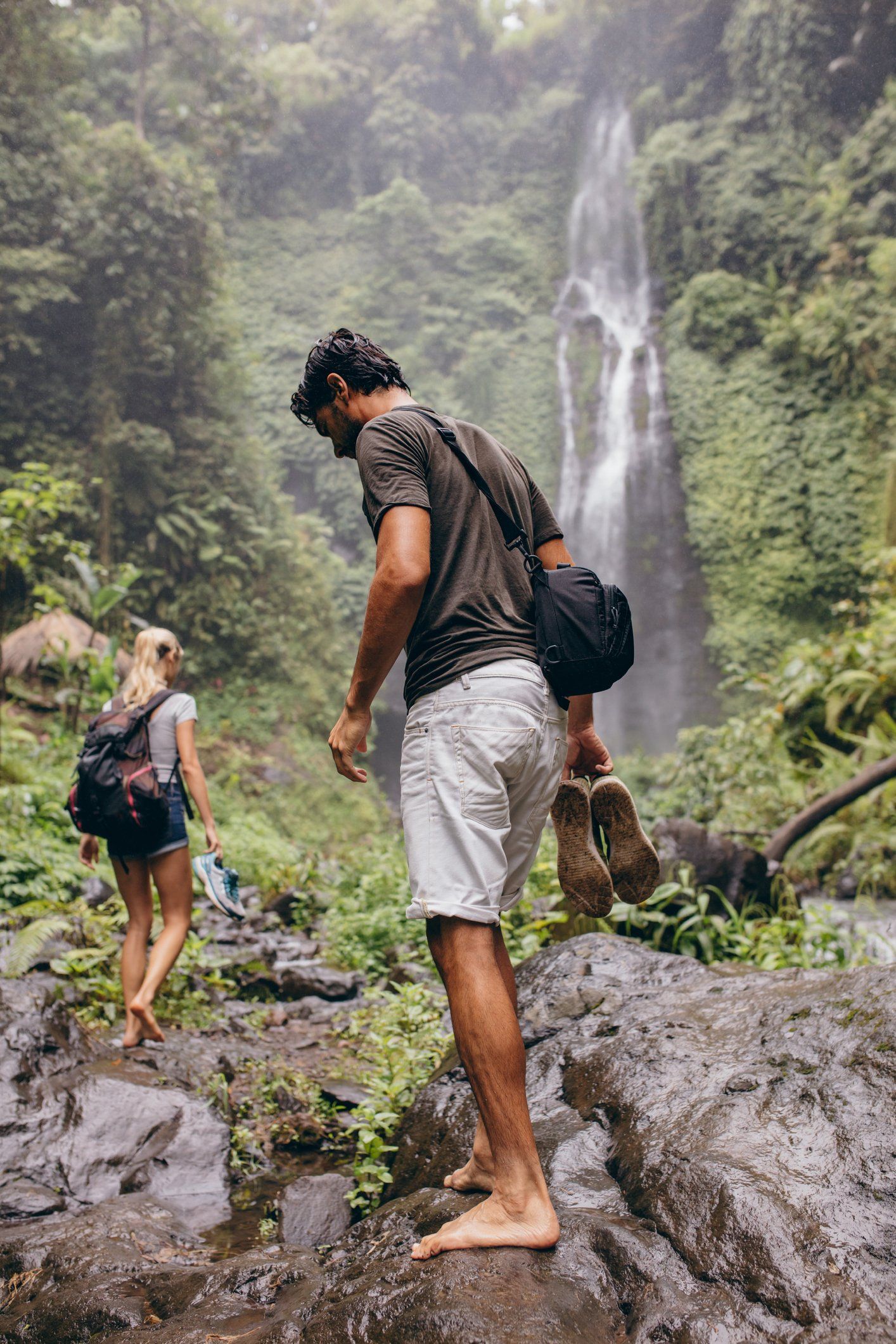 A man and a woman are hiking in the woods near a waterfall.