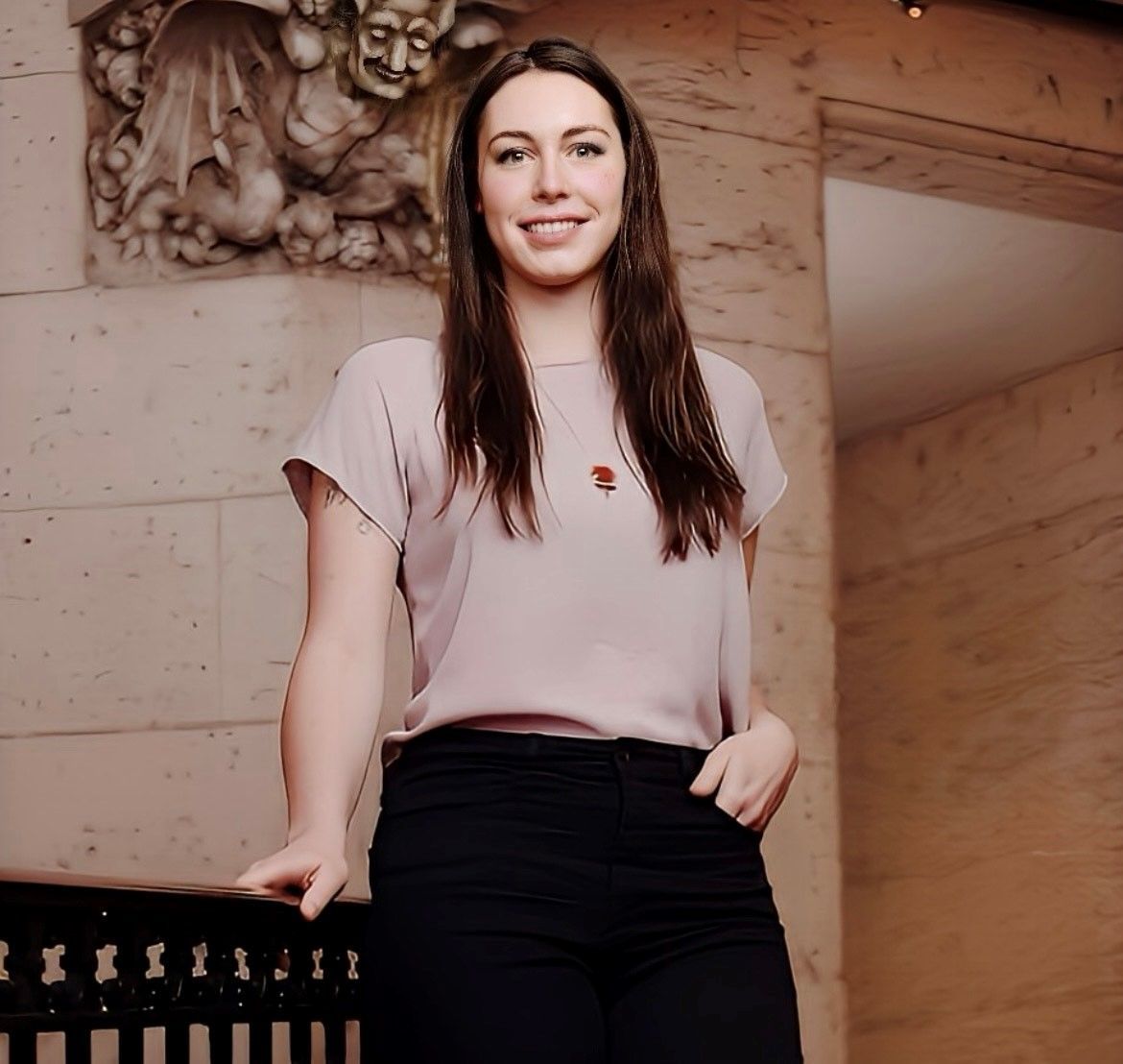 A woman in a pink shirt and black pants stands in front of a statue