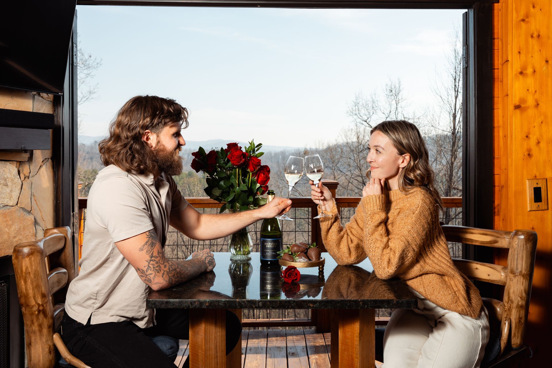 Two champagne glasses clink in front of a fireplace, filled with bubbles, hands raised in toast.