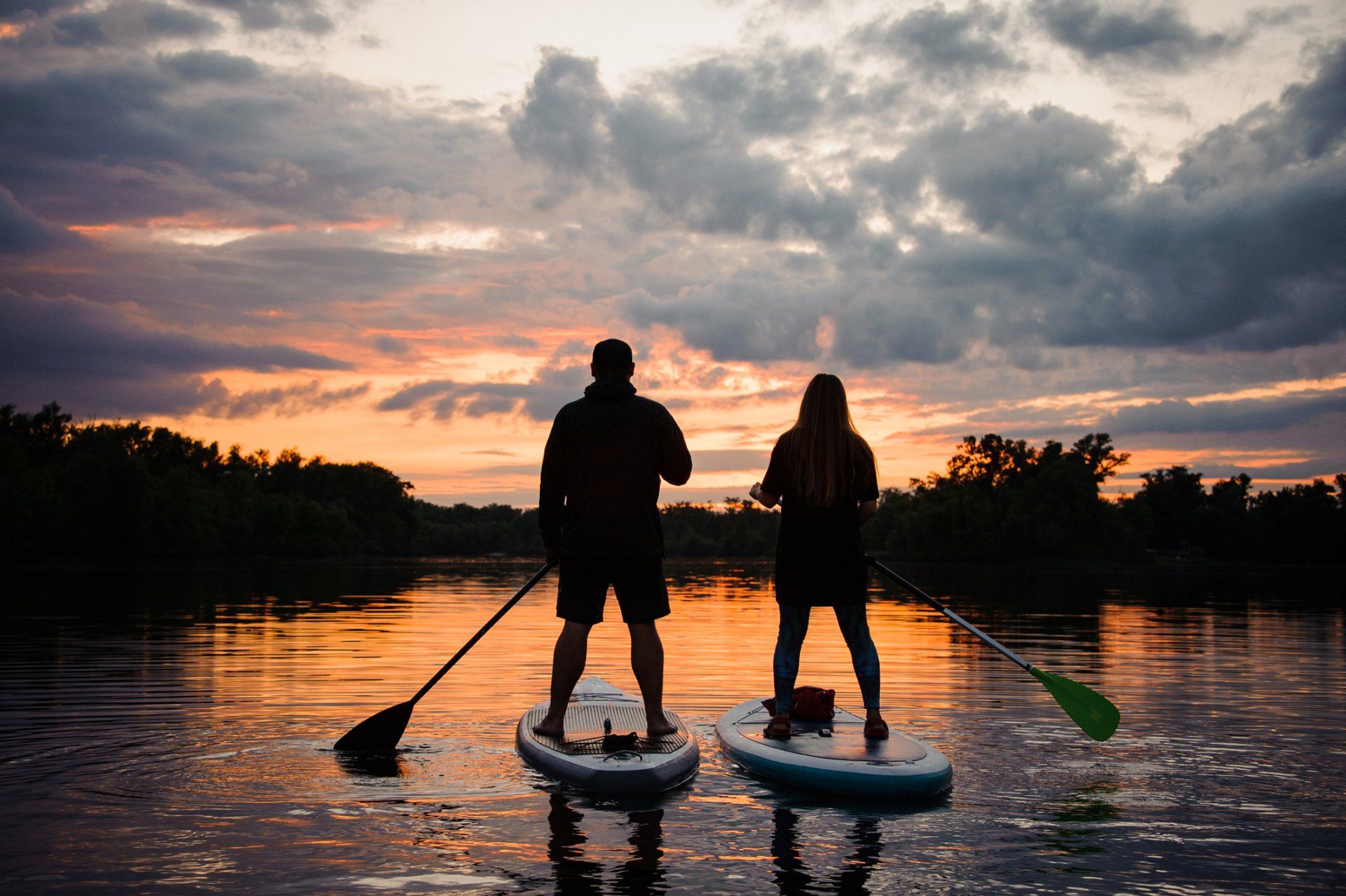 a man and a woman are standing on paddle boards in the water at sunset .