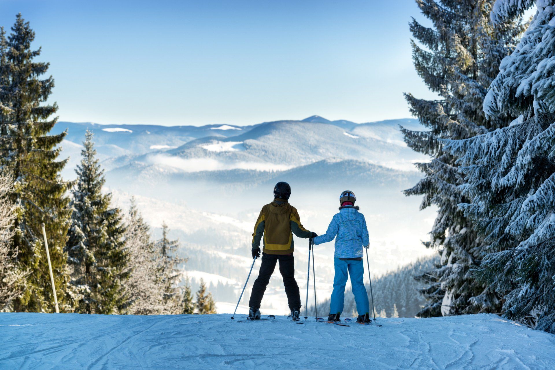 Two people are standing on top of a snow covered slope holding hands.