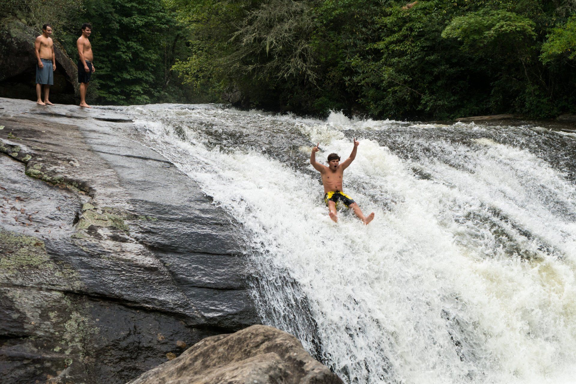 A man is sliding down a waterfall with his arms in the air.