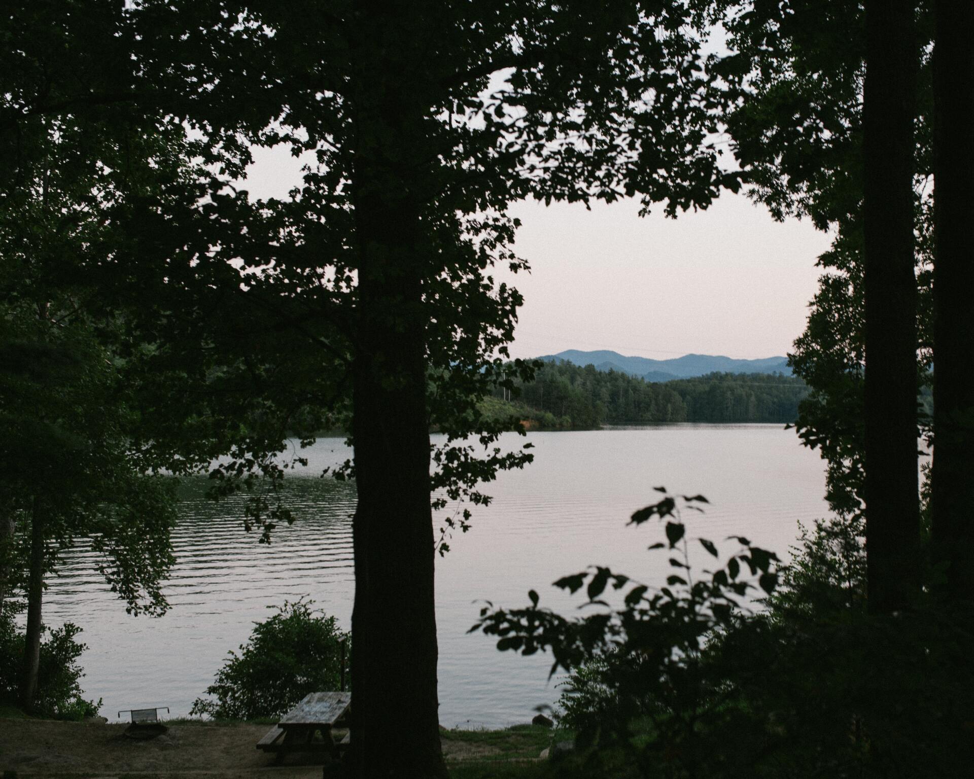 A lake surrounded by trees with a picnic table in the foreground