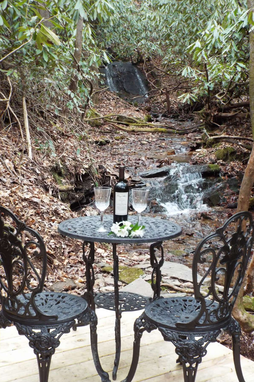 A table with a bottle of wine and two glasses on it in front of a waterfall.