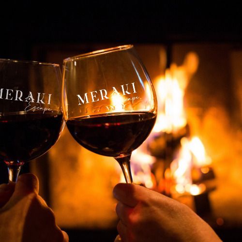 Two hands toasting with wine glasses in front of a fireplace, the glasses are labeled