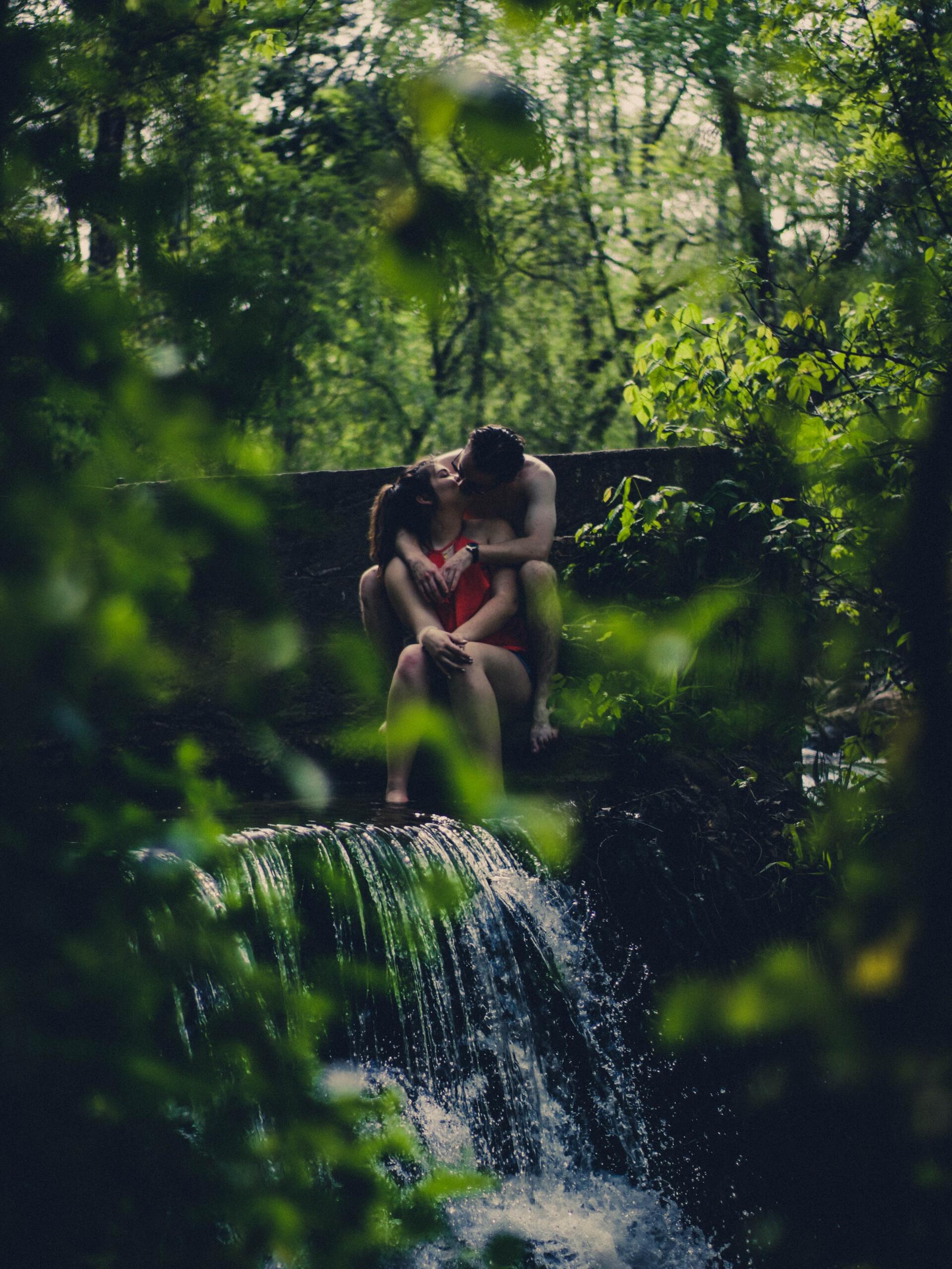 a man and a woman are sitting next to a waterfall in the woods .