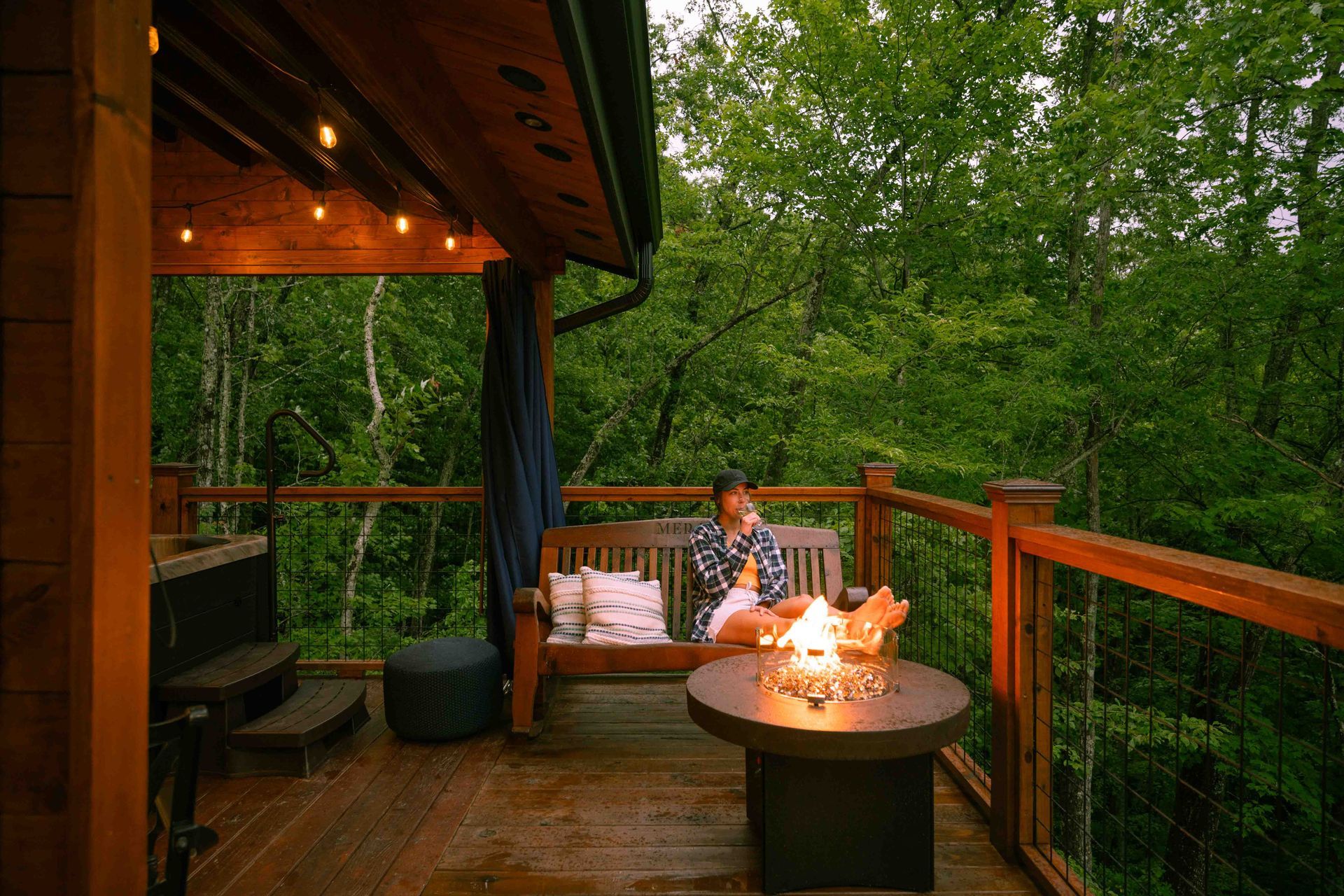 A woman is sitting on a bench on a deck next to a fire pit.
