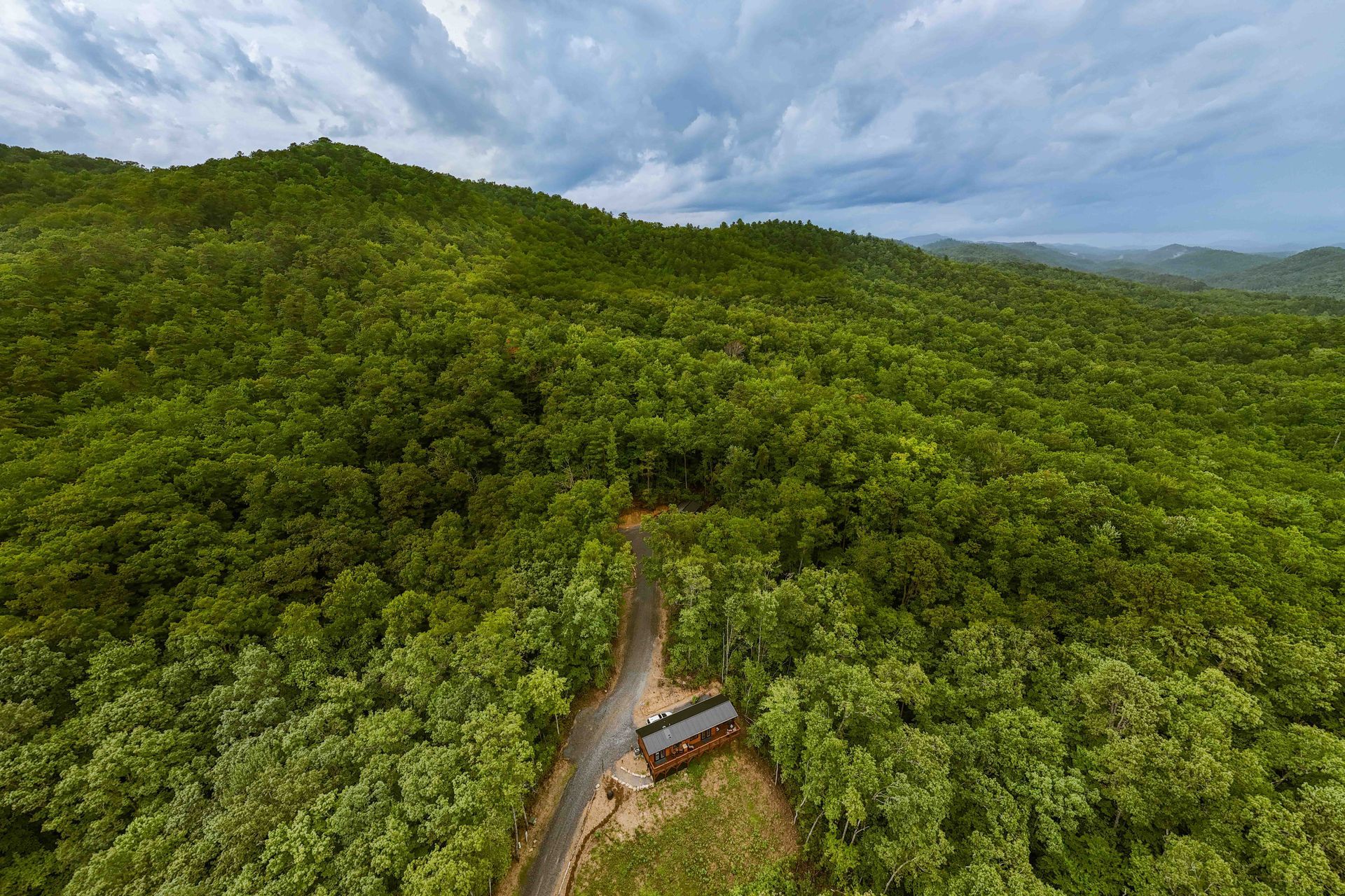 A winding road through dense green forest under a cloudy sky.