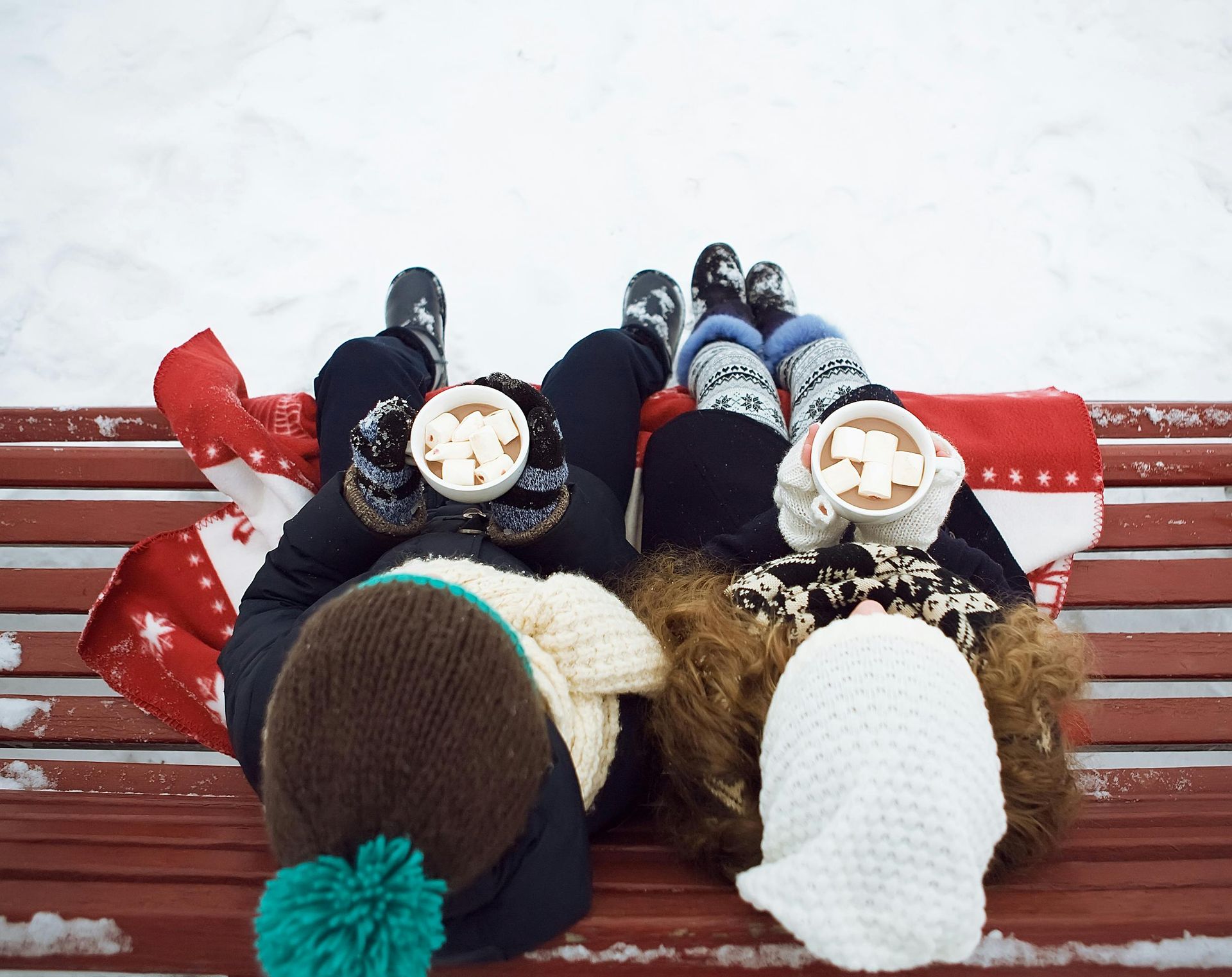 Two people laying on a bench holding cups of hot chocolate