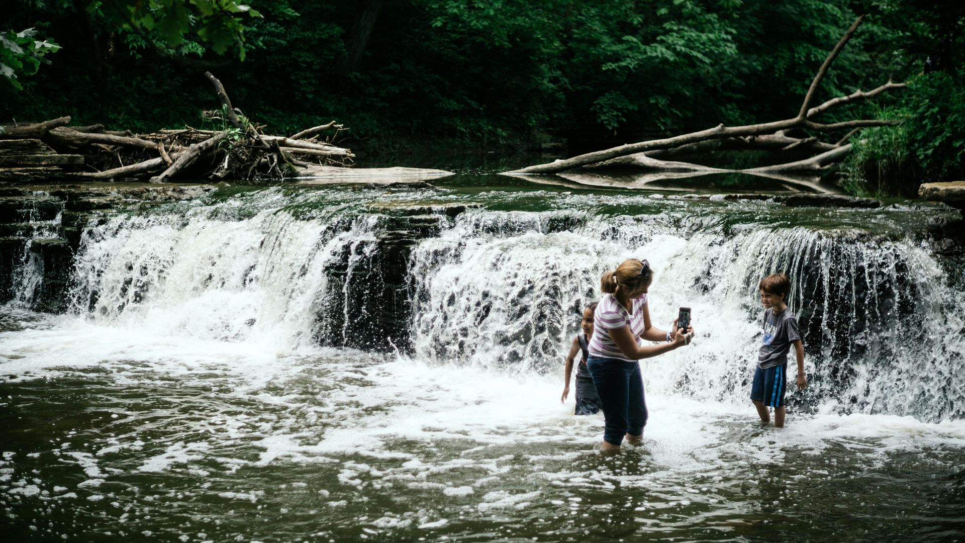 A woman and a child are standing in front of a waterfall.