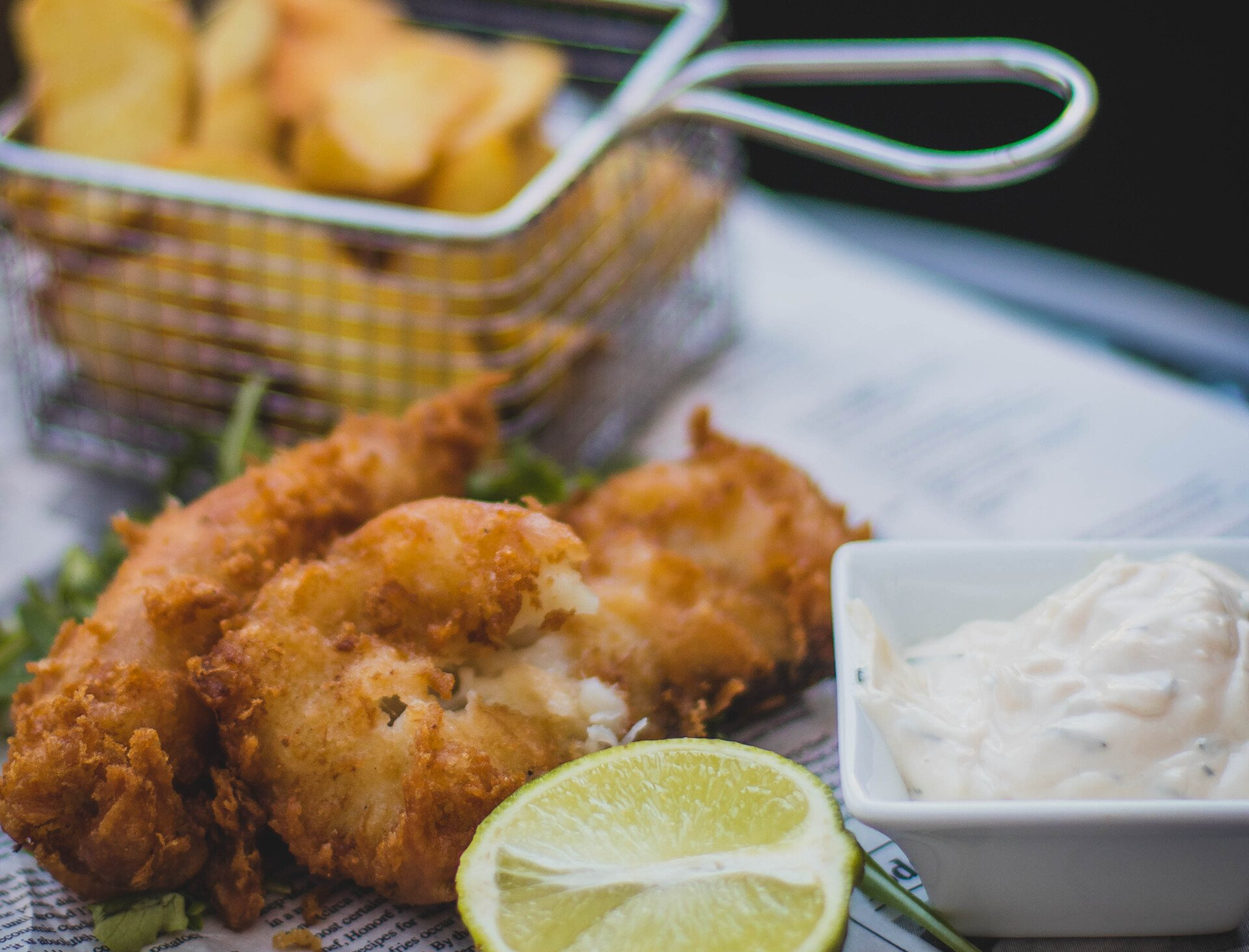 A plate of fish and chips with a slice of lime and a bowl of dipping sauce.