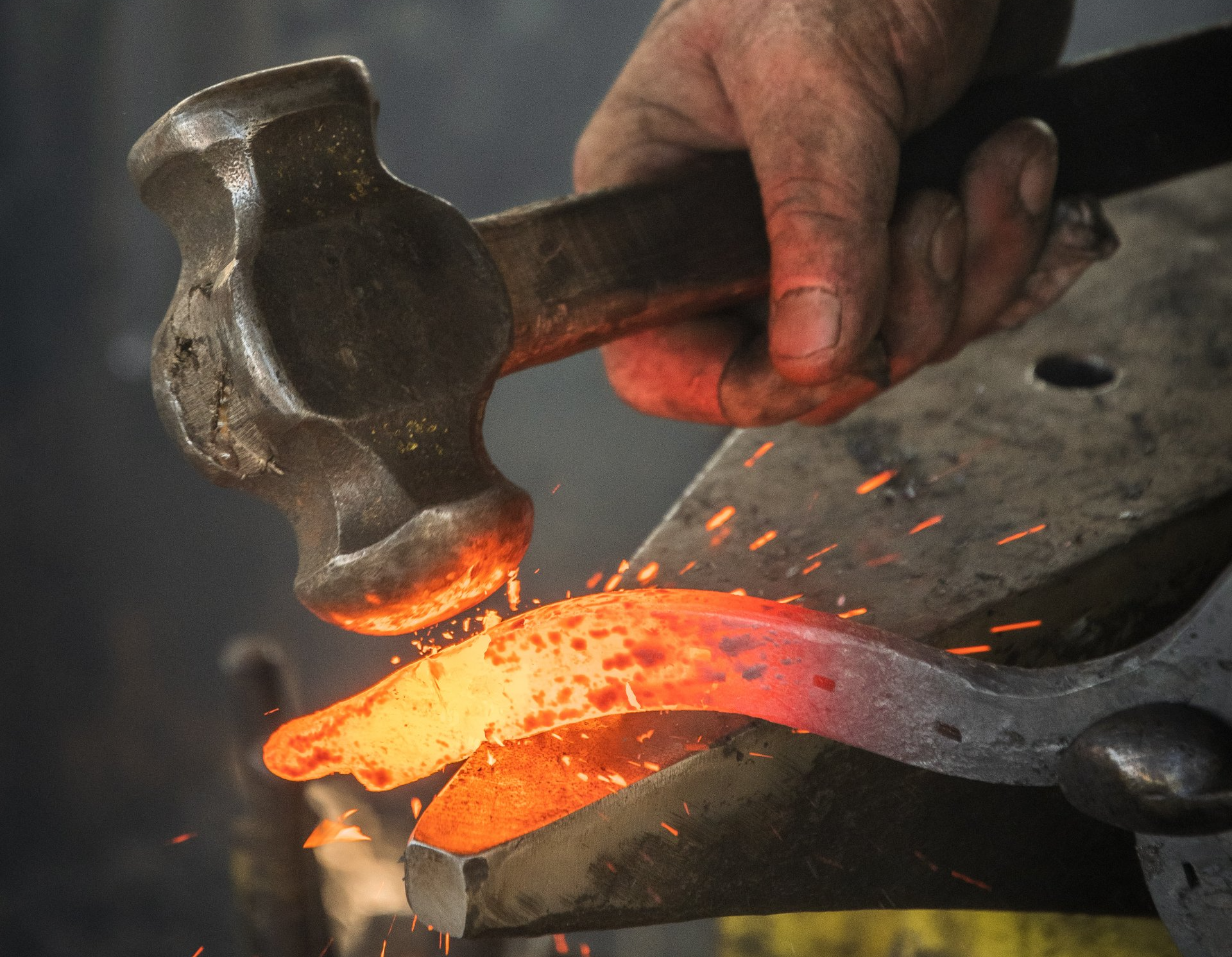 A person is holding a hammer over a piece of hot metal