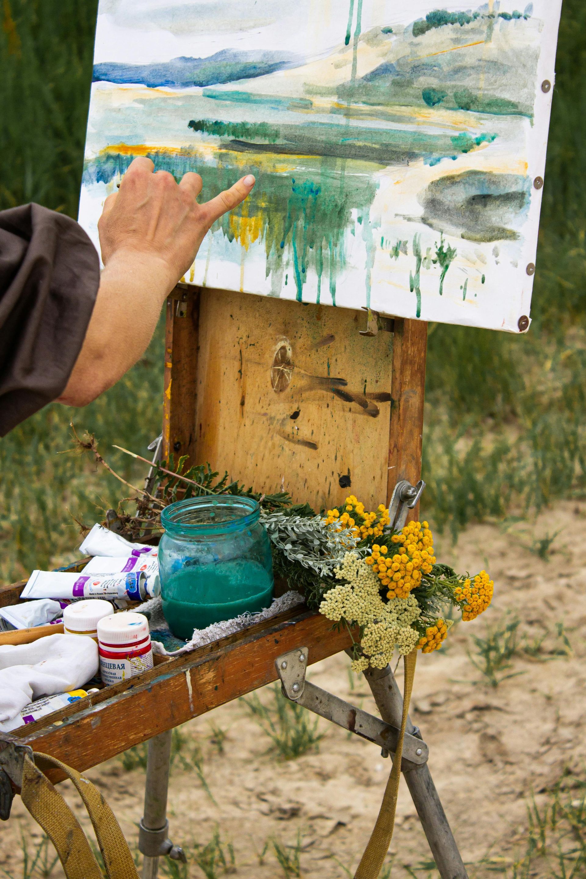 A person is pointing at a painting on an easel.