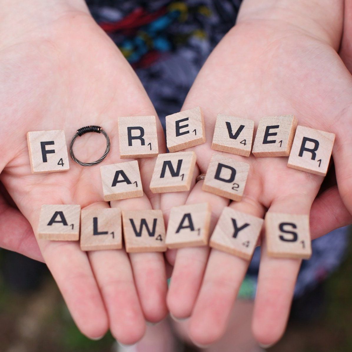 A person is holding scrabble tiles that say forever and always