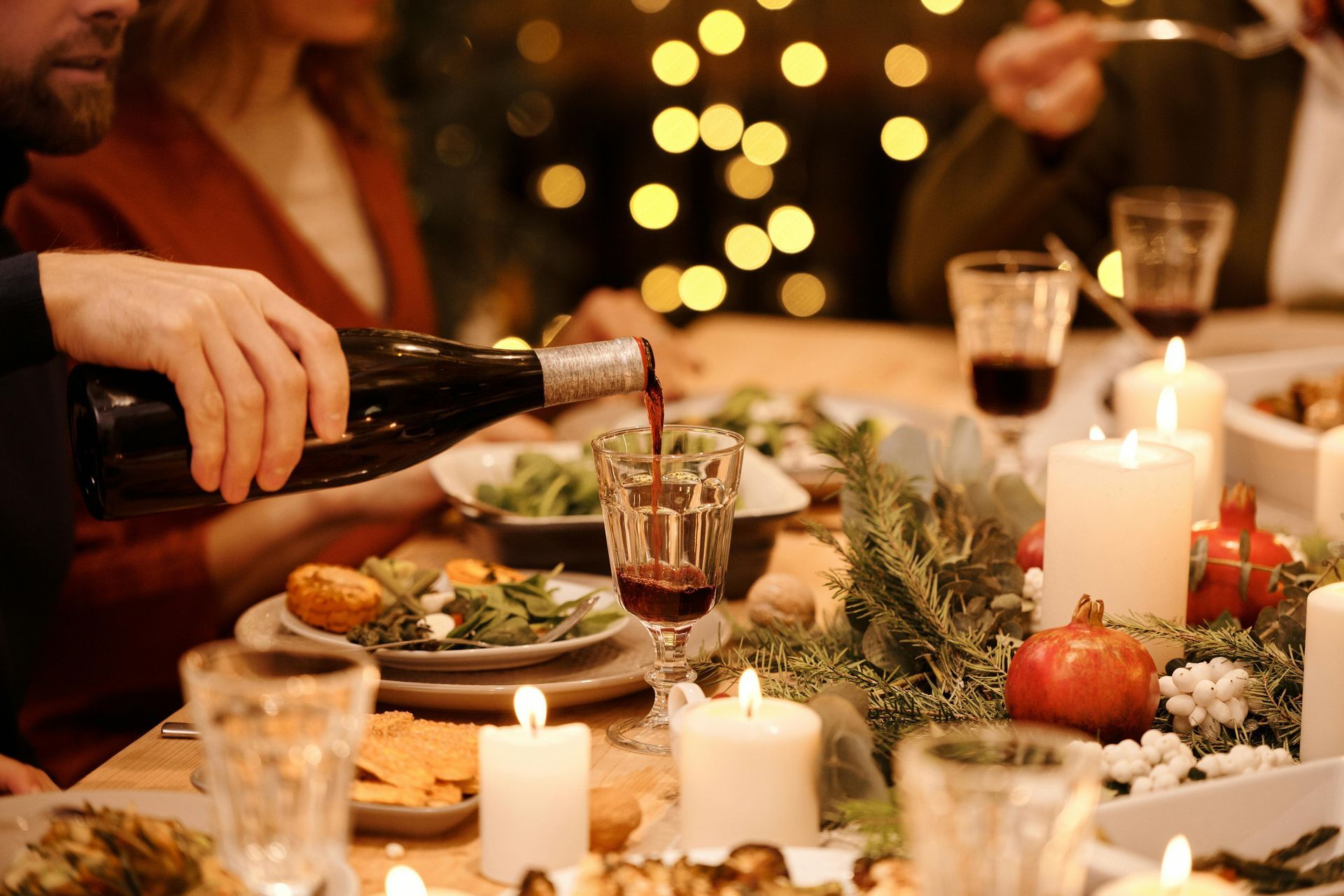 A man is pouring wine into a glass at a christmas dinner table.