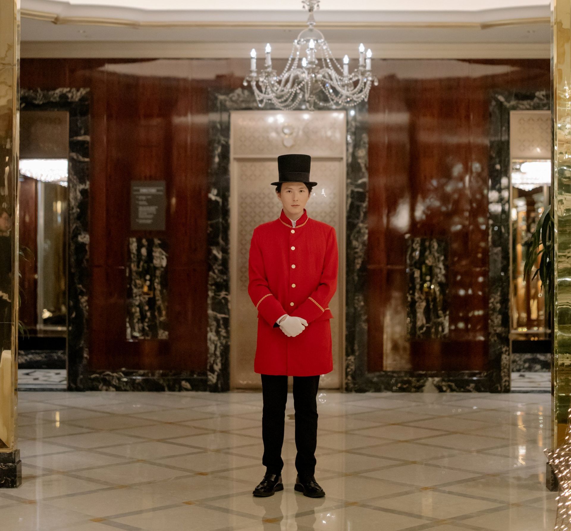 A man in a red coat and top hat stands in front of an elevator