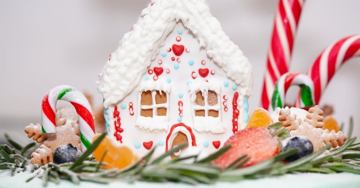 A gingerbread house is sitting on top of a cake with candy canes and fruit.