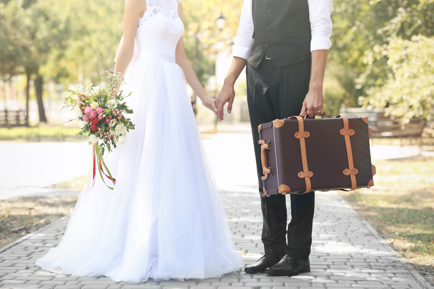 A bride and groom are holding hands while holding a suitcase.