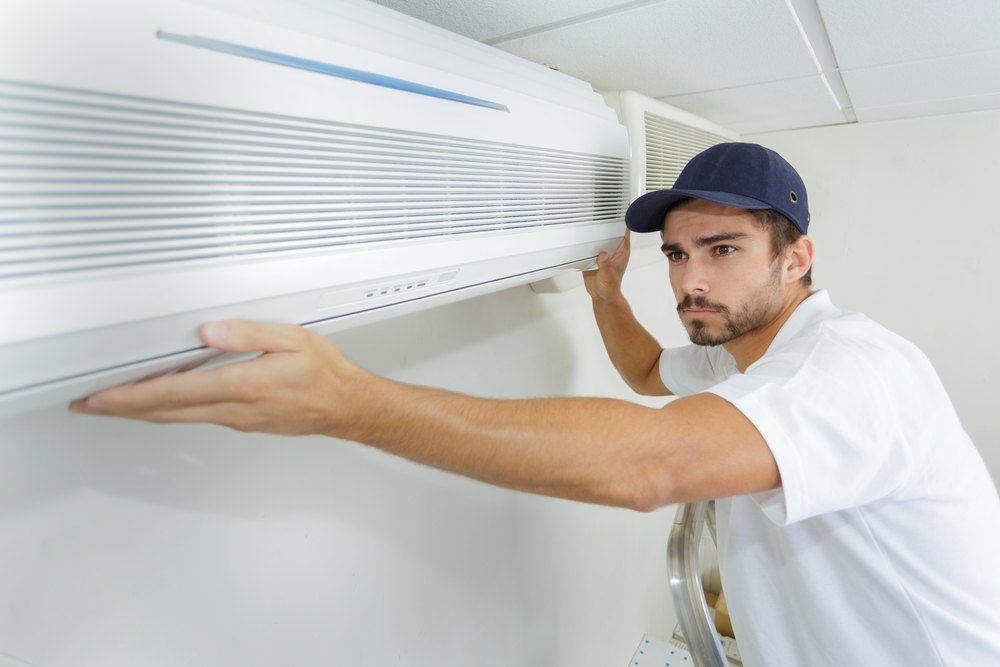 A Man is Installing an Air Conditioner on a Wall — Action Air N Elec in Maroochydore, QLD
