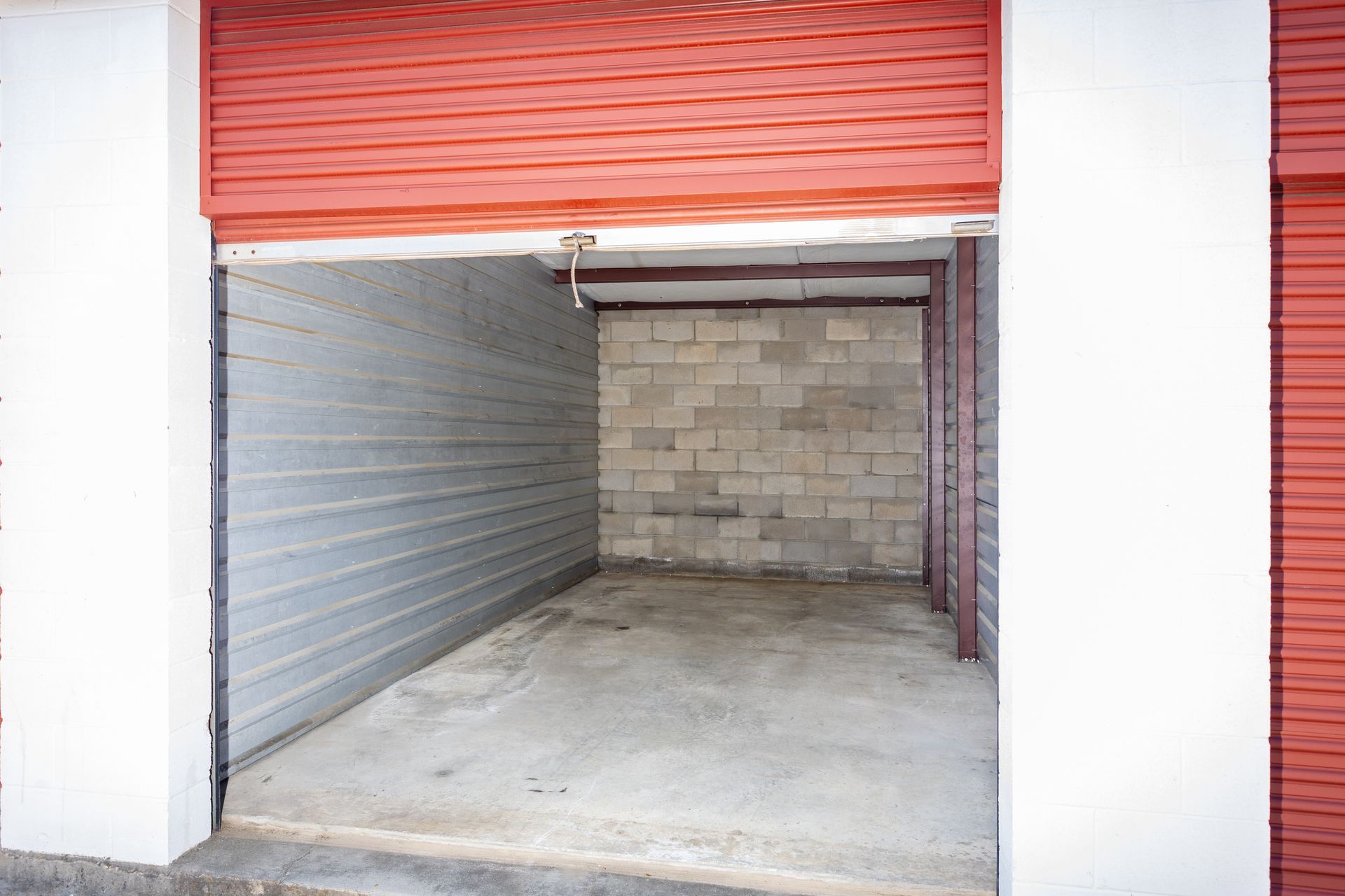 Storage unit with red door rolled up, interior with concrete block wall.
