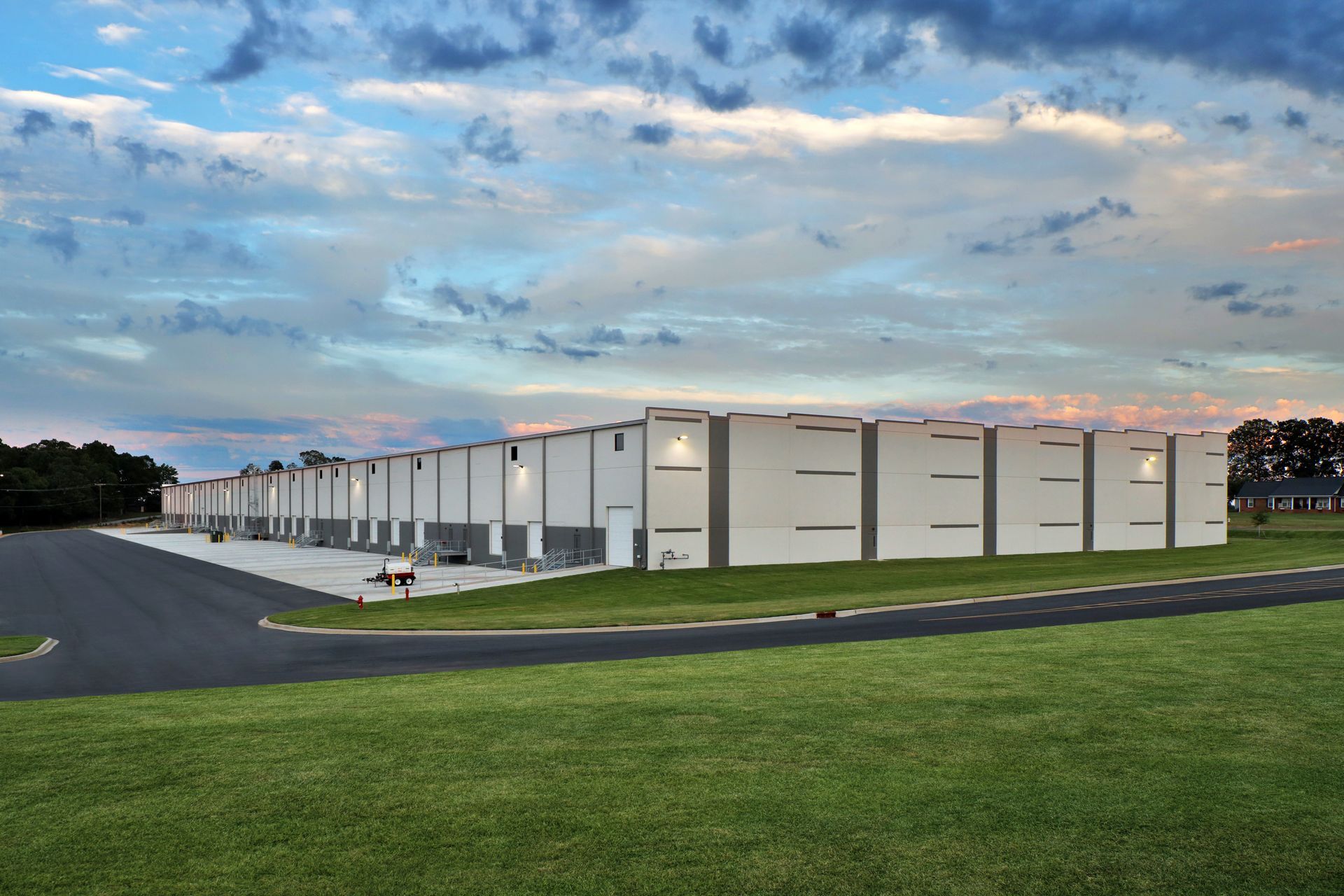 Long, gray industrial building under a cloudy blue sky. Grass and asphalt in foreground.