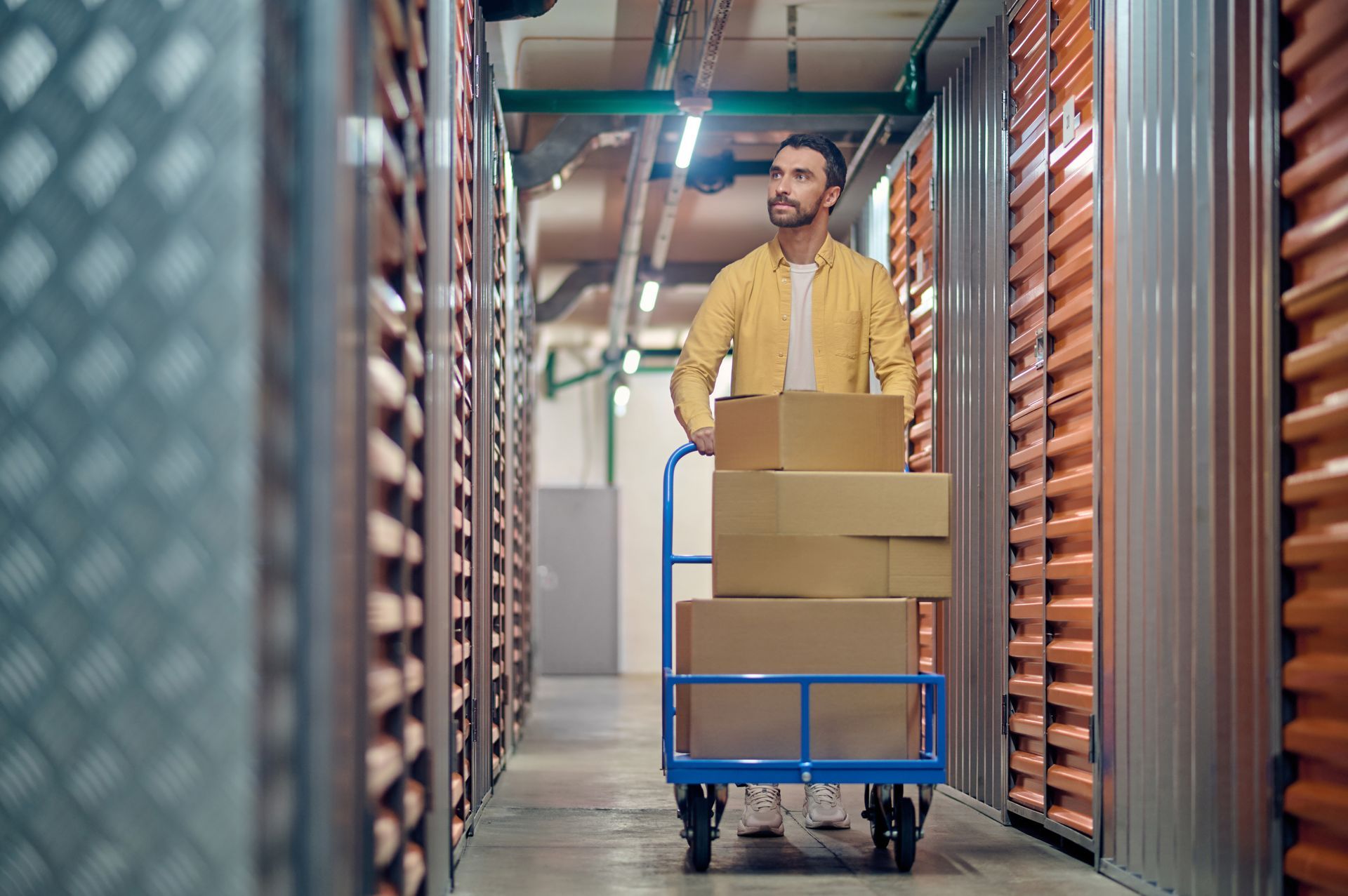 Man pushing a hand truck with boxes down a storage unit hallway.