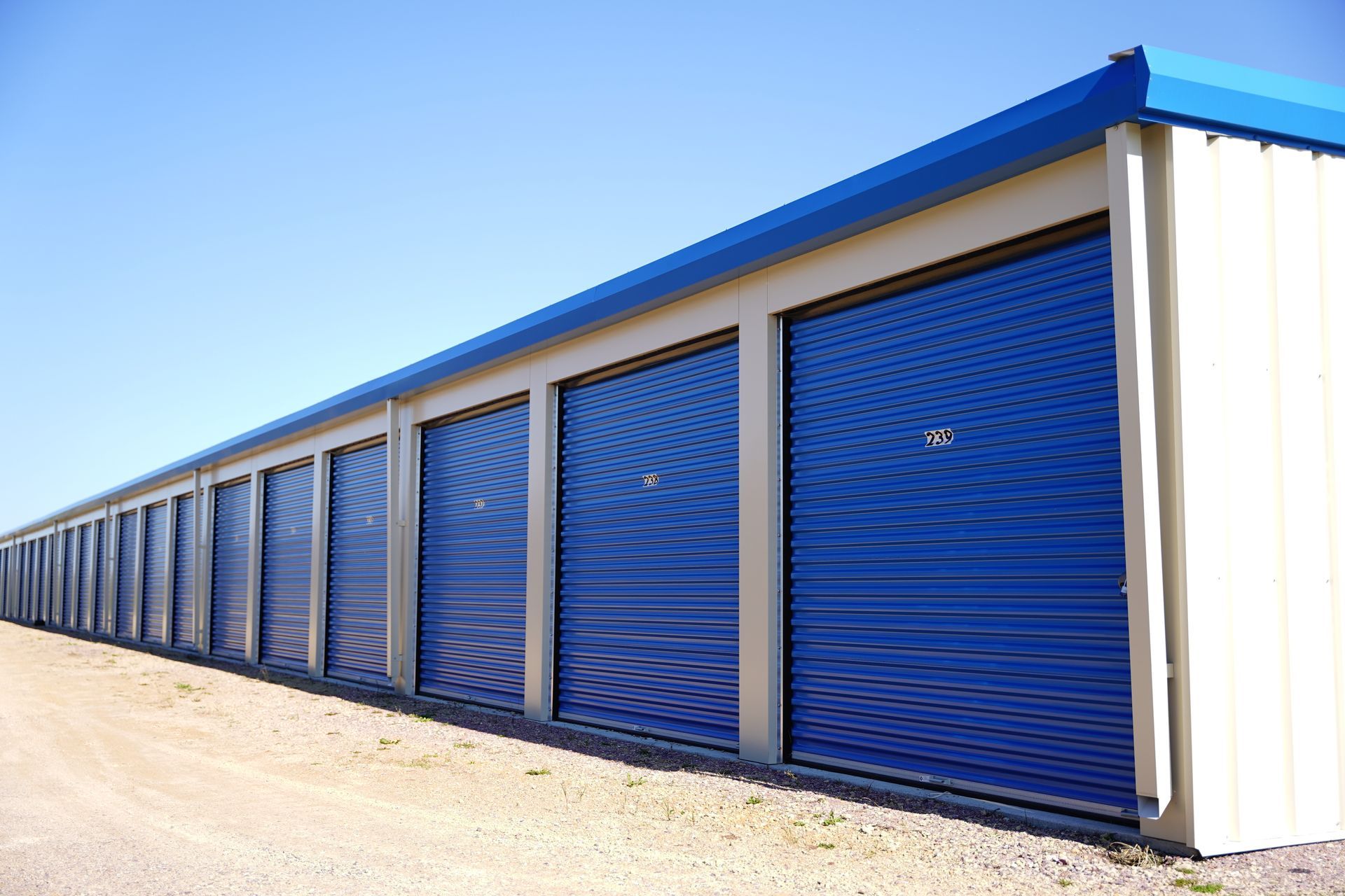 Storage unit hallway with red doors and silver accents. Shiny floor, overhead lights.