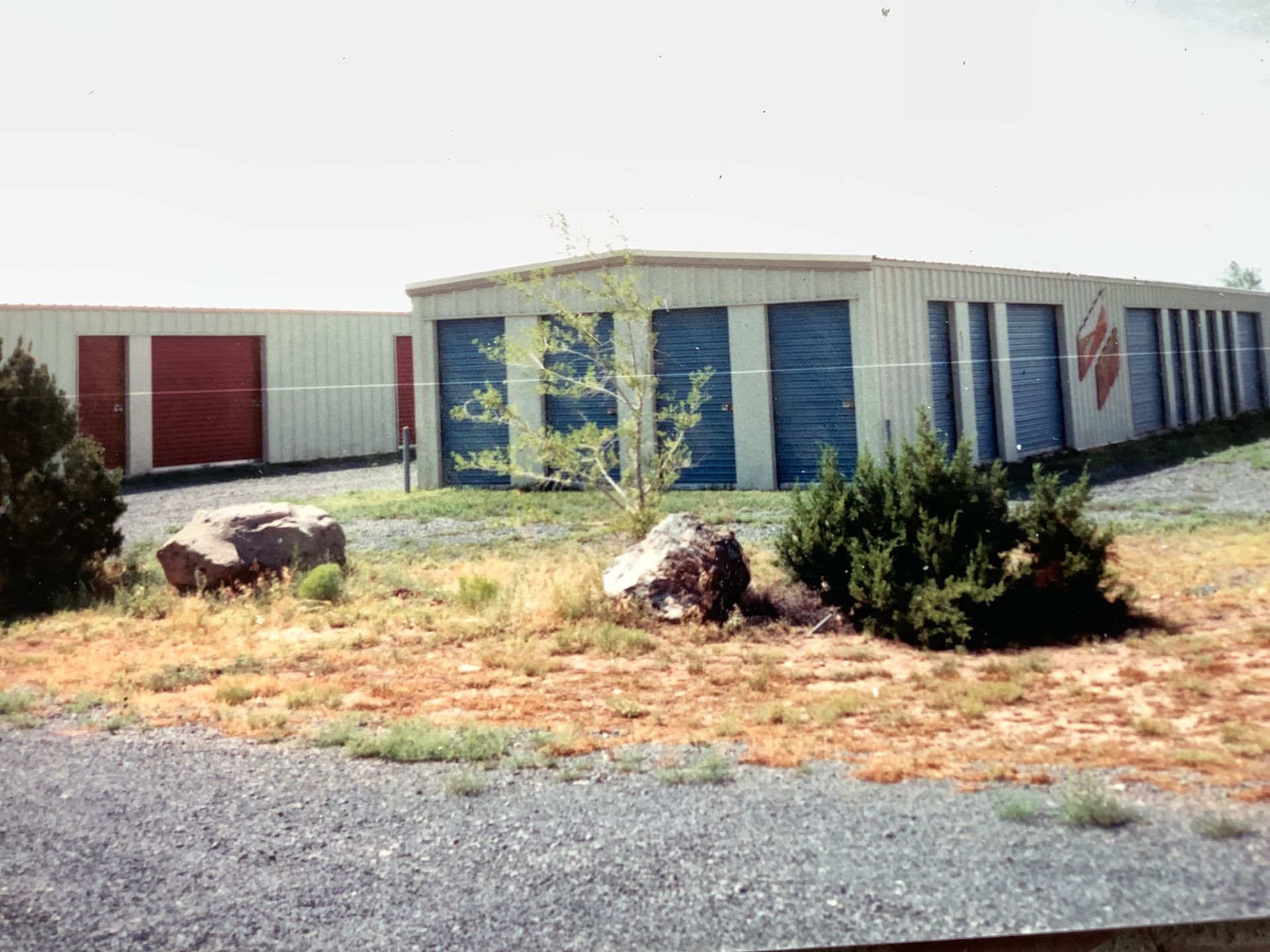 Blue storage unit door open, revealing cardboard boxes inside. Brick wall, concrete floor.