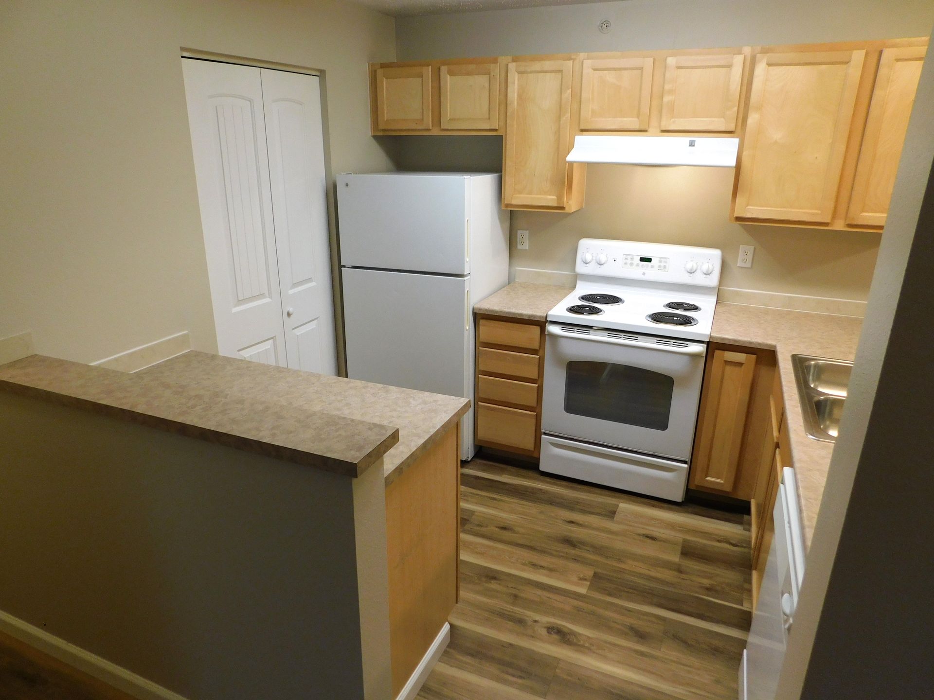 Small kitchen with wood cabinets, white appliances, and a breakfast bar.