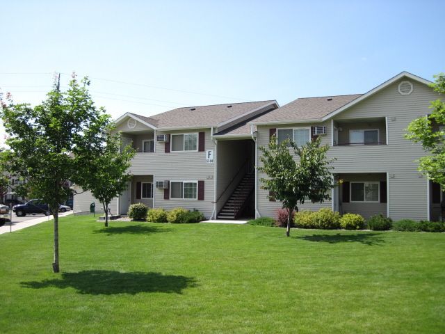 Apartment complex with light siding, brown roof, and green lawn under a clear blue sky.