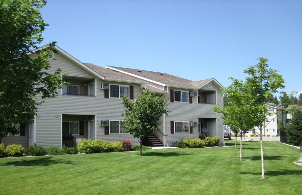 Two-story apartment building with tan siding and a grassy lawn under a blue sky.