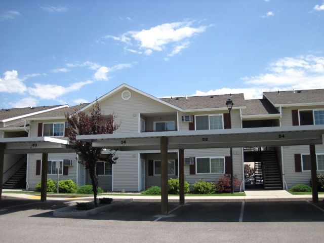 Apartment complex with light siding, covered parking, and blue sky.