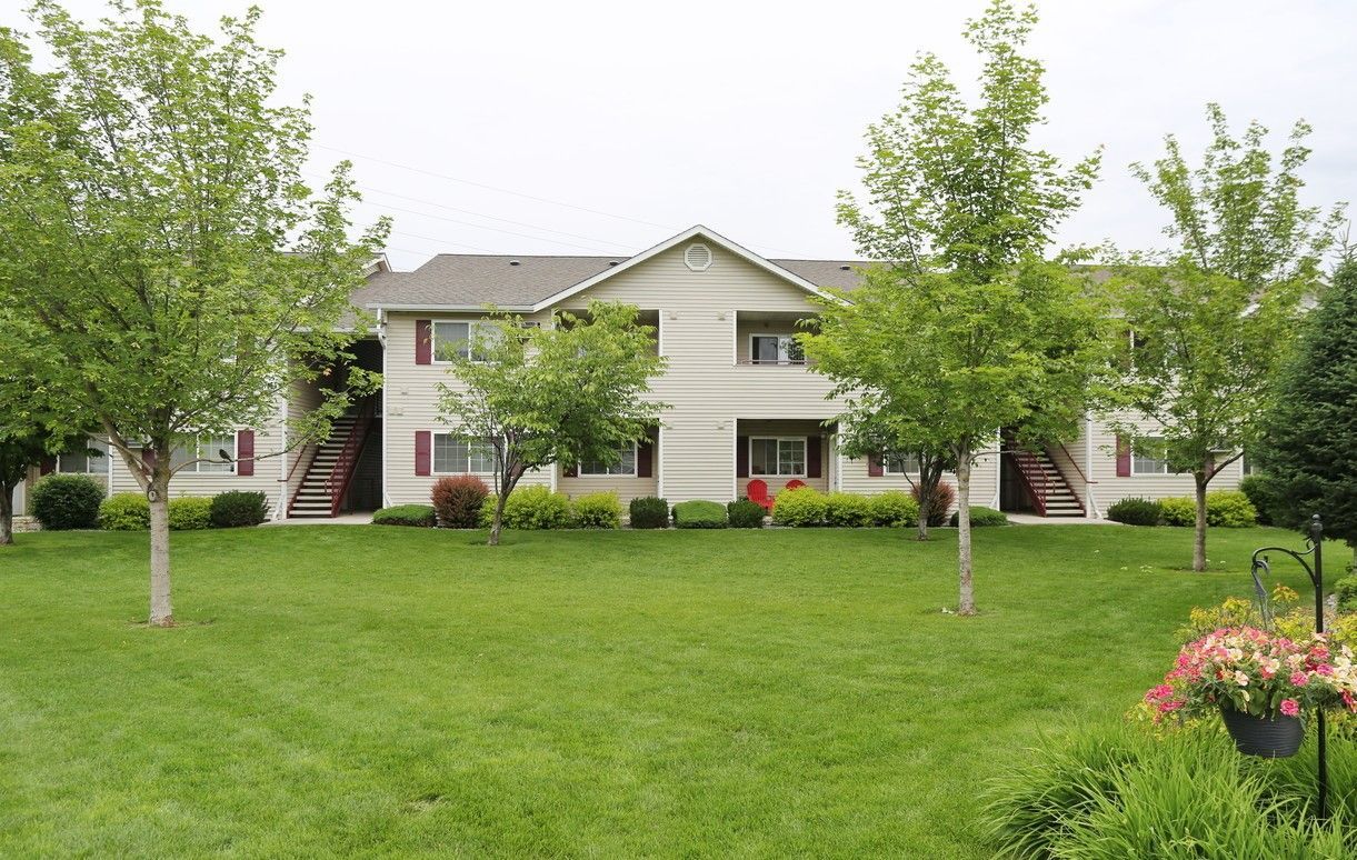 Apartment building with green lawn, trees, and bushes.