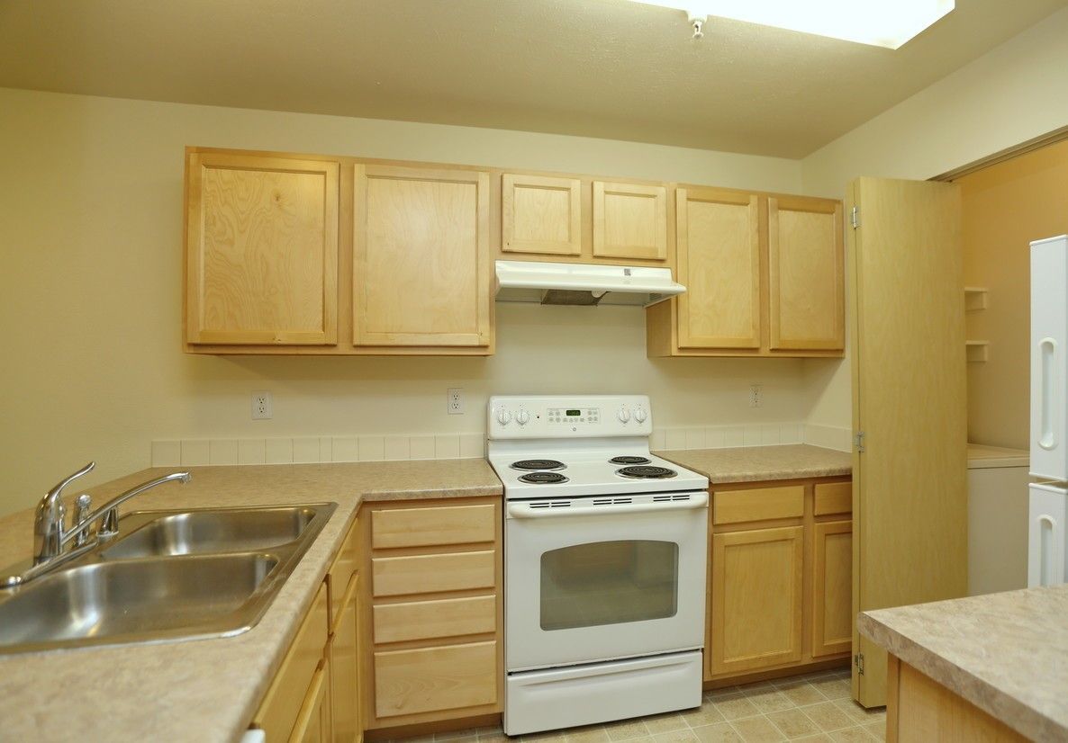 A kitchen with light wood cabinets, white appliances, and beige countertops.
