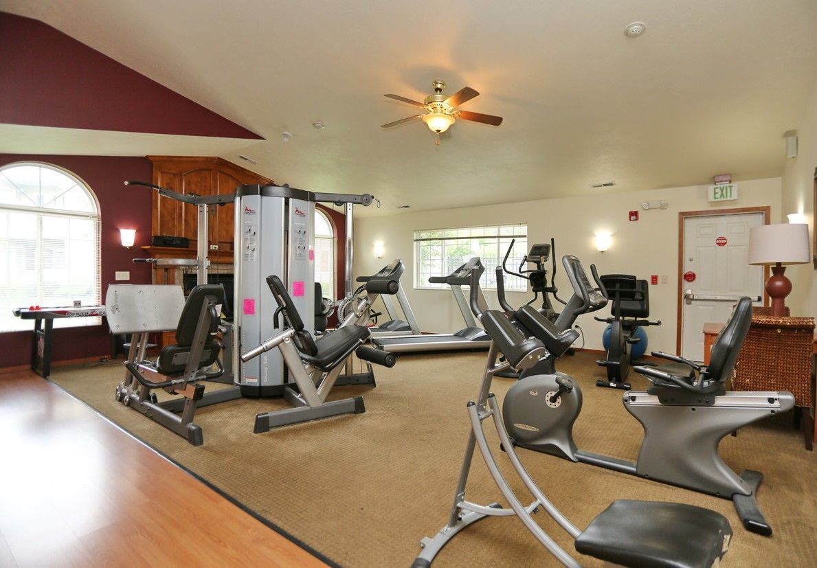 Gym with exercise machines, beige carpet, and burgundy ceiling accents.