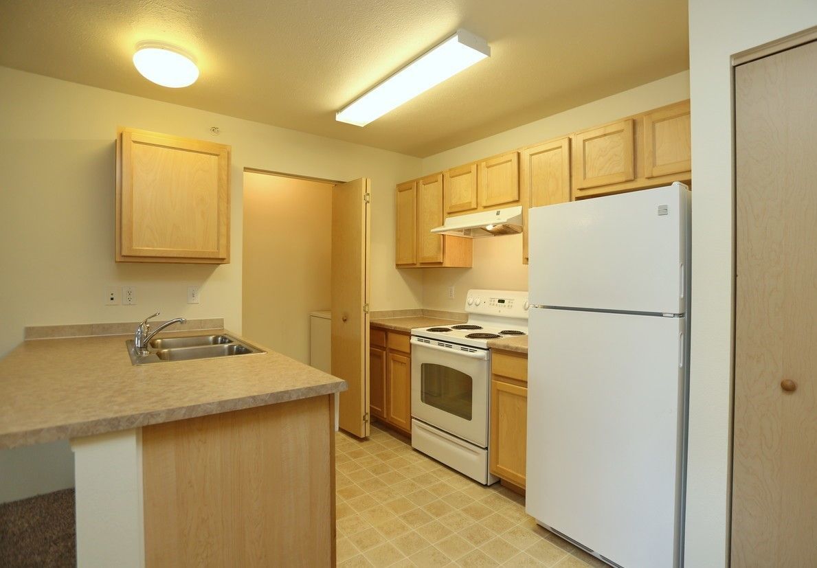 Kitchen with light wood cabinets, white appliances, and beige countertops and flooring.