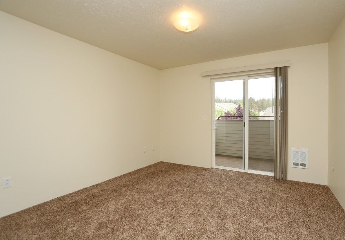 Empty room with brown carpet, sliding glass door to balcony, and off-white walls.