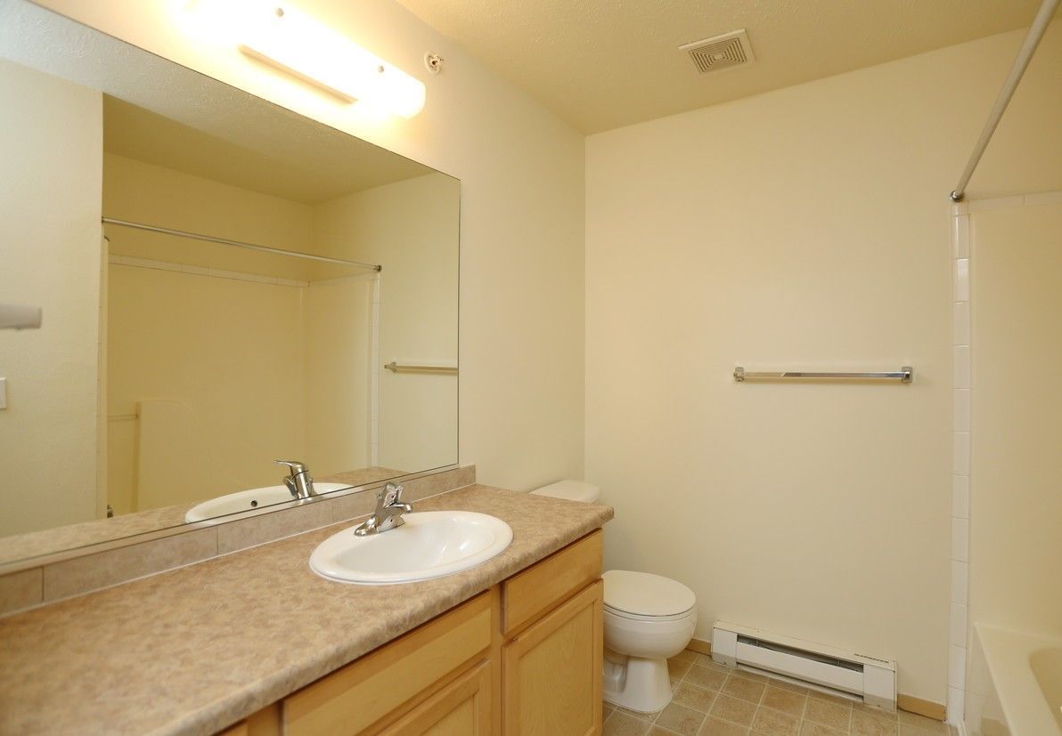 Bathroom with beige walls, beige countertop, white sink, toilet, and tub, a mirror, and a towel rack.